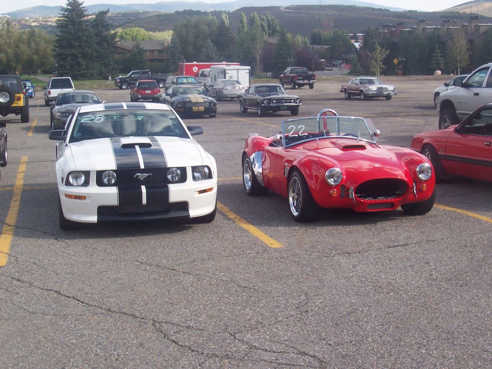 White Ford Mustang with black stripes and red Cobra sports car with number 22 on windshield