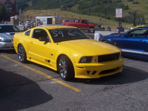1972 Ford Ranchero - A bright yellow Ford Mustang is parked in a lot, possibly at a car show or race event, with other vehicles nearby.
