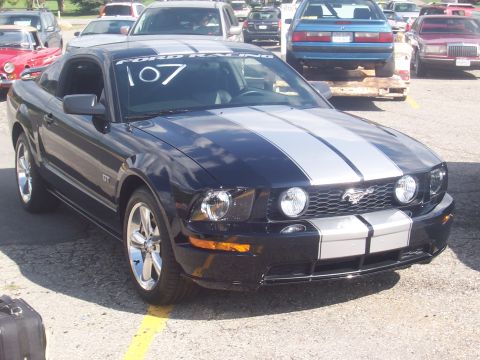 1972 Ford Ranchero - Black 2005 Ford Mustang GT with racing stripes parked in a lot with other vehicles.