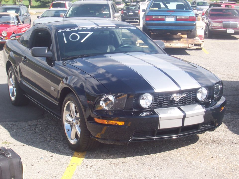 Black Ford Mustang GT with silver racing stripes, number 107 on windshield. Other cars visible in background