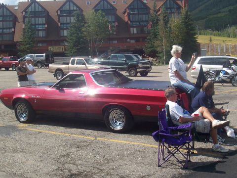 1972 Ford Ranchero - A red 1972 Ford Ranchero pickup truck is parked in a lot with people sitting nearby.