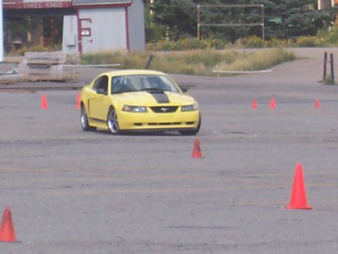 1972 Ford Ranchero - A yellow 2000 Ford Mustang with black racing stripes is seen on a paved course marked with orange cones.