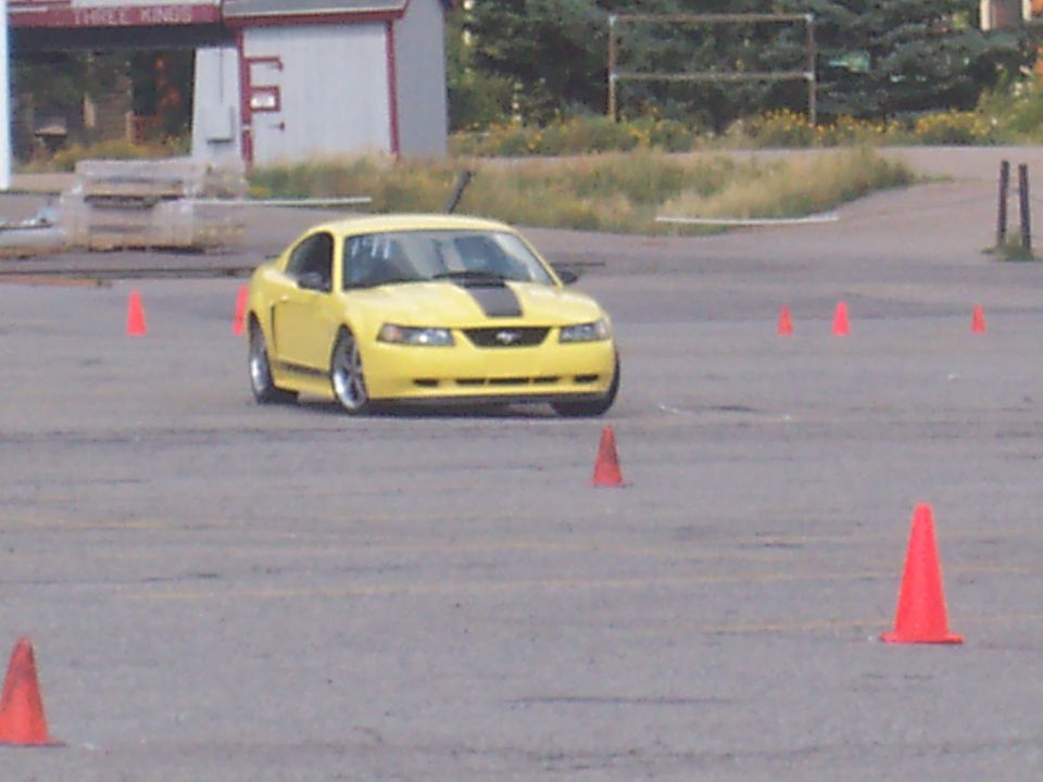 Yellow 2000 Ford Mustang with black racing stripes navigating a cone course