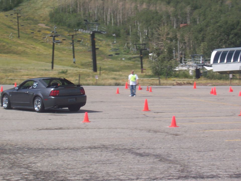 Dark coupe with a spoiler and racing number '15' on the fender, parked on asphalt with orange cones
