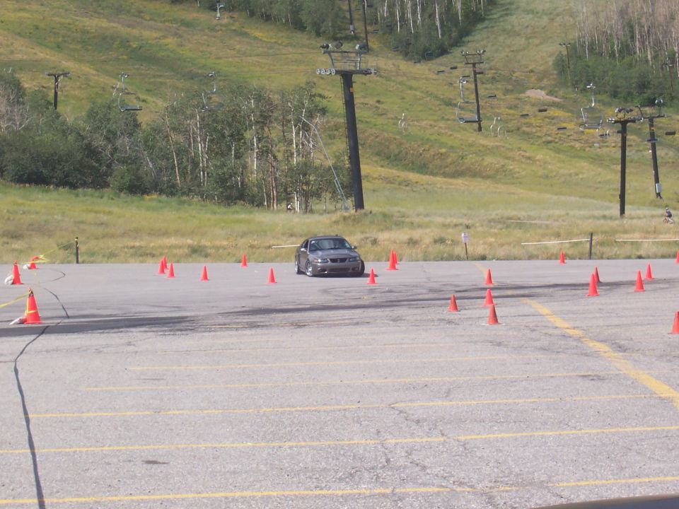 Car navigating a cone course on a paved lot with ski lifts in the background