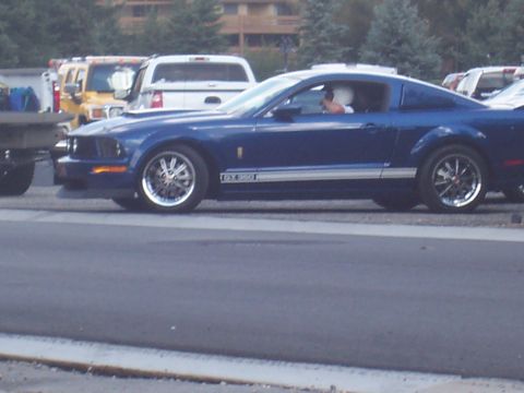 1972 Ford Ranchero - A blue coupe with white racing stripes is seen from the side, with other vehicles in the background.