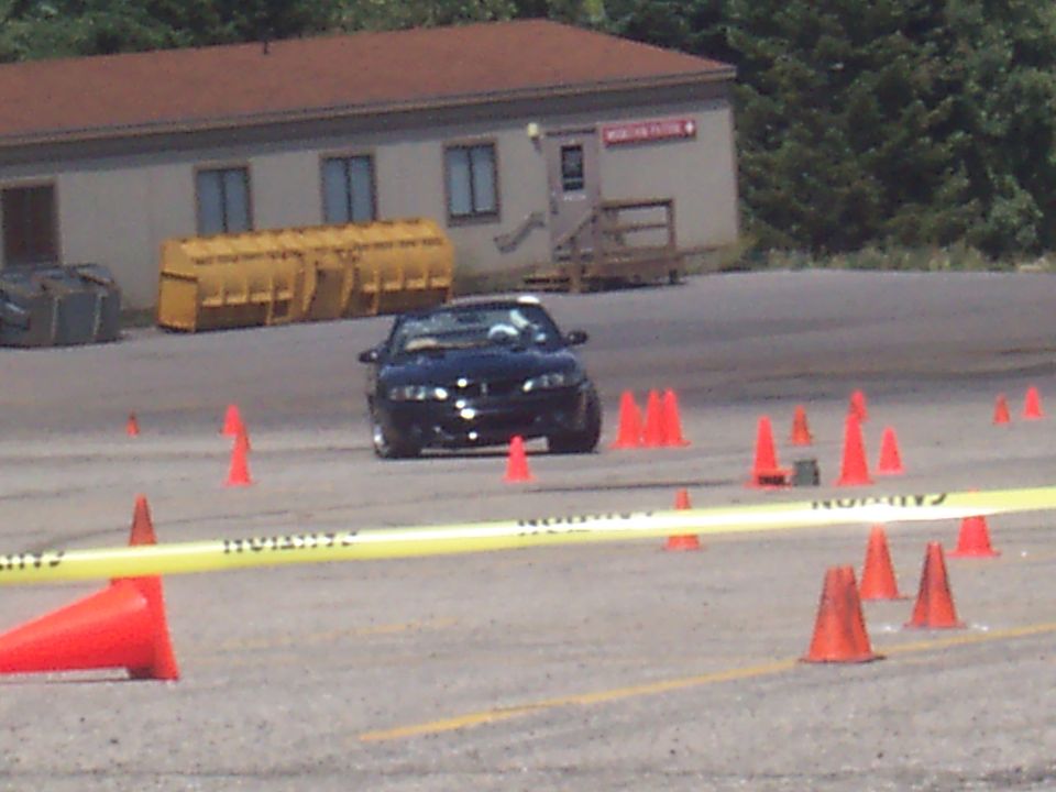 Black sports car navigating an obstacle course marked by orange cones and yellow caution tape