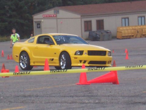 1972 Ford Ranchero - A yellow Ford Mustang is positioned on a course marked by cones and caution tape, with a building in the background.