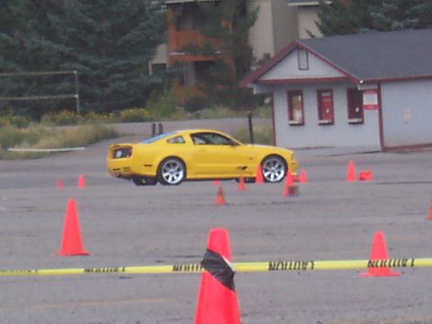 1972 Ford Ranchero - A yellow sports coupe is seen from the side driving through a course marked by orange cones and caution tape.