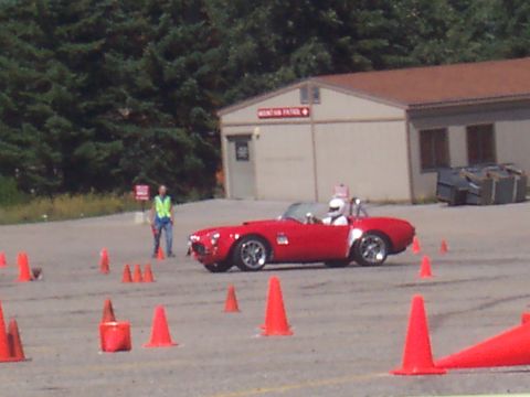 1972 Ford Ranchero - A red convertible sports car navigates a course marked by orange cones, with a building in the background.