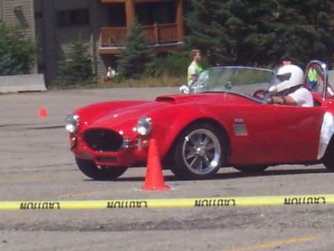 1972 Ford Ranchero - A driver in a helmet pilots a red convertible sports car through a course with cones and caution tape.