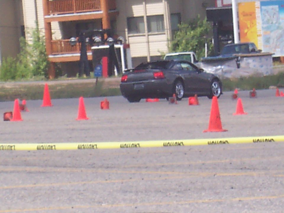 Dark convertible coupe seen from rear, surrounded by orange cones
