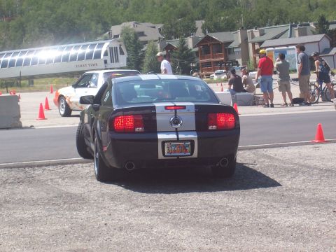 1972 Ford Ranchero - Rear view of a black Ford Mustang with silver racing stripes parked outdoors.
