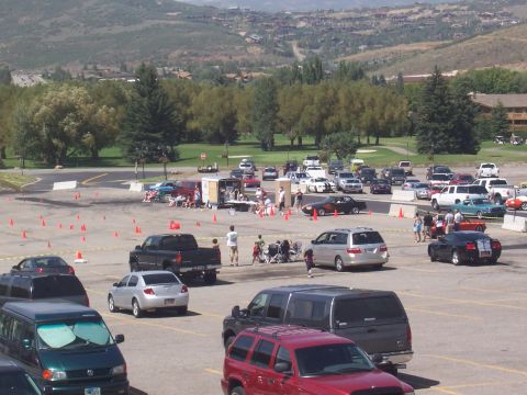 1972 Ford Ranchero - A busy parking lot hosts an event with numerous vehicles and spectators gathered around a central trailer.