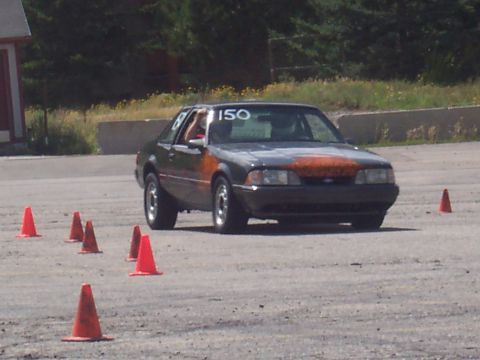 1972 Ford Ranchero - A dark gray coupe with an orange hood and racing number 150 navigates a course marked by orange cones.