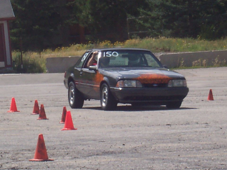 Dark gray coupe with orange hood and racing number 150 on windshield, seen from the front