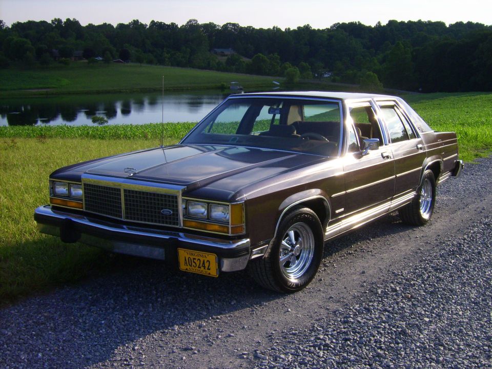 Dark brown Ford LTD Crown Victoria sedan front three-quarter beside a farm pond