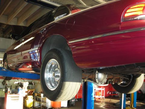 1992 Ford Crown Victoria - A maroon sedan is raised on a car lift, revealing its undercarriage and rear wheel assembly.