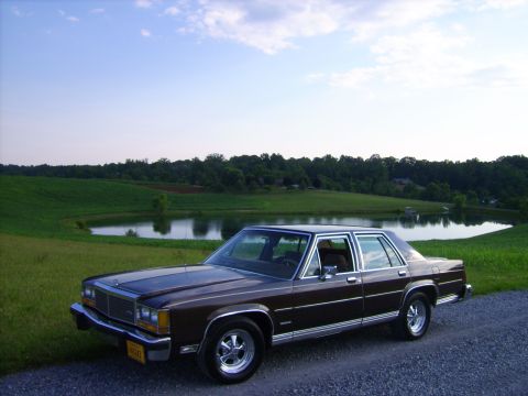 1982 Ford LTD Crown Victoria - Dark brown Ford full-size four-door sedan parked on a gravel edge above a farm pond, shot from a high 3/4 front angle with green pasture an…