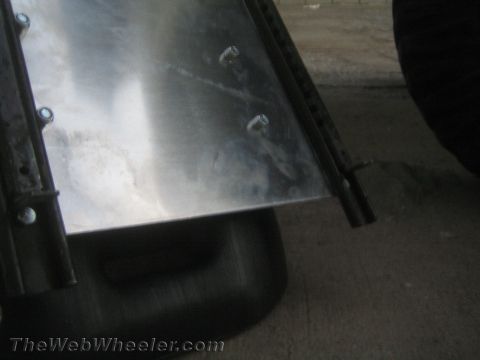1987 Suzuki Samurai - A metal panel is bolted to a black frame, with a dark object below and a tire visible on the right.