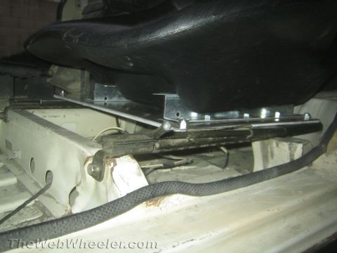1987 Suzuki Samurai - Close-up of a seat mounting bracket and frame rail under a black vinyl seat in a stripped vehicle interior.
