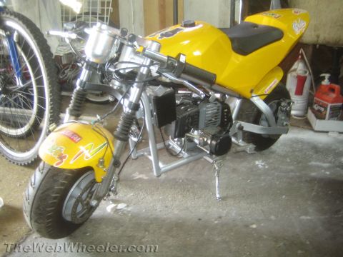 1968 Ford Mustang - A yellow pocket bike is parked indoors next to a bicycle wheel and some containers.