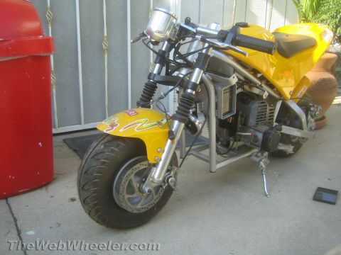1968 Ford Mustang - A yellow pocket bike is parked on a concrete surface next to a red trash can.