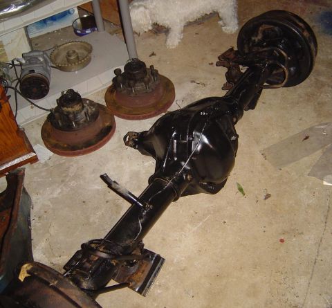 1986 Ford Bronco - A black rear axle assembly with attached brake rotors and hubs is displayed on a concrete floor.