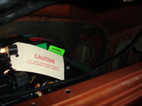 1977 Ford F-150 - Caution tag on coolant lines in engine bay warns of pressure and advises careful cap removal.