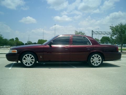 2004 Ford Crown Victoria - Side profile of a maroon sedan parked in a lot under a cloudy sky.