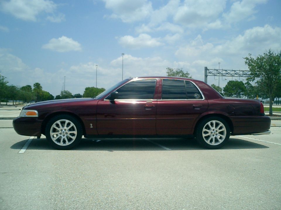 Maroon sedan parked on pavement, side view. It looks like a 2004 Ford Crown Victoria