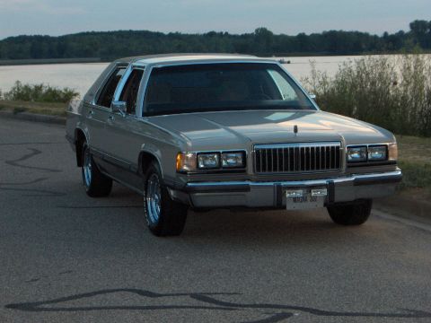 1988 Mercury Grand Marquis - A 1988 Mercury Grand Marquis sedan is parked by a lake under a cloudy sky.