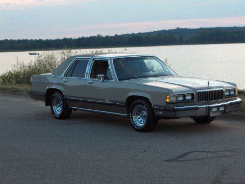 1988 Mercury Grand Marquis - A 1988 Mercury Grand Marquis sedan is parked on the side of the road next to a body of water.