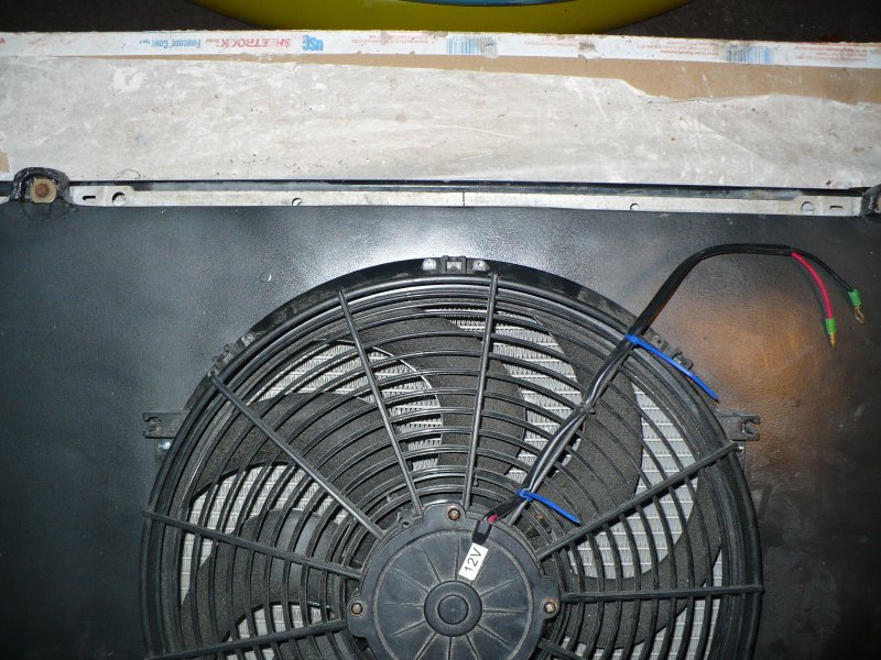Electric fan mounted on a radiator with visible wiring and a '12V' label