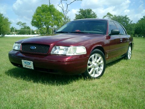 2004 Ford Crown Victoria - A maroon Ford Crown Victoria is parked on a grassy field under a partly cloudy sky.