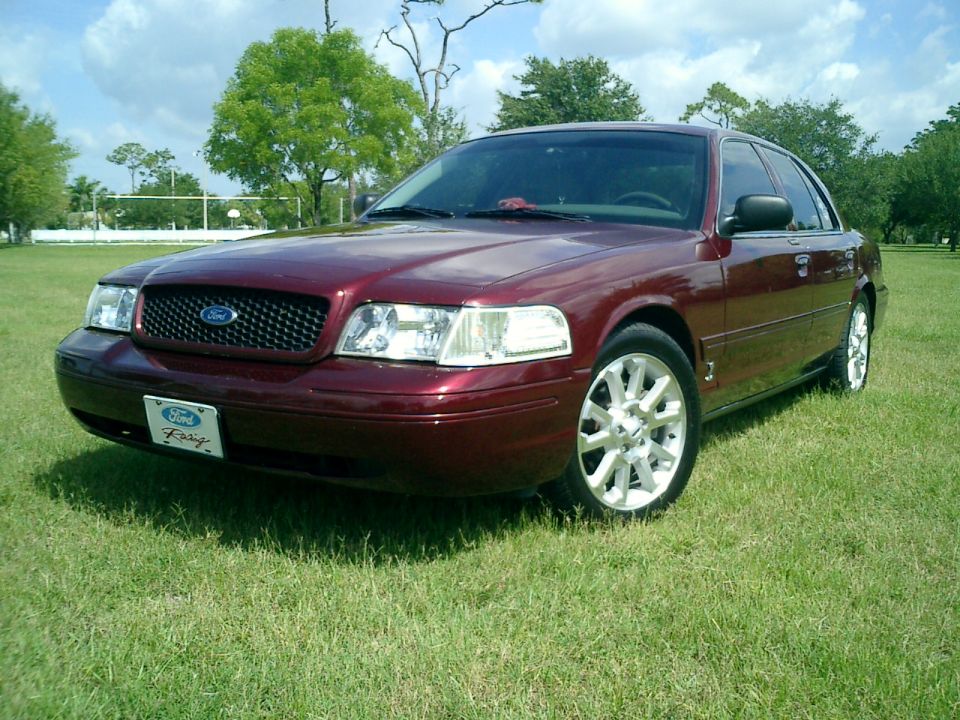 Maroon Ford Crown Victoria parked on grass, front 3/4 view, showing grille and headlights