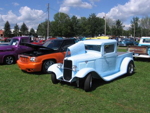 1989 Ford Mustang - A light blue hot rod pickup truck with custom flame decals is parked on a grassy field alongside other vehicles.