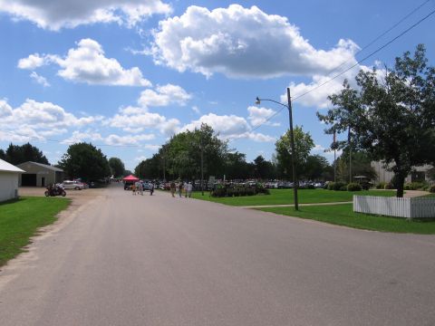 1989 Ford Mustang - Outdoor gathering with many vehicles and attendees on a sunny day with scattered clouds.