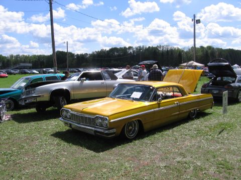 1989 Ford Mustang - A gold candy-painted 1964 Chevrolet Impala hardtop sits slammed on wire-spoke lowrider wheels with whitewall tires on a grass show field, t…