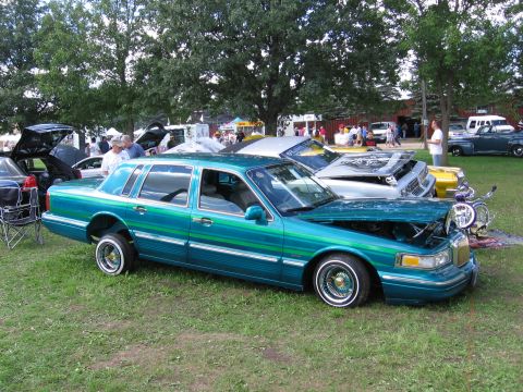 1989 Ford Mustang - A customized sedan with a unique paint job is displayed outdoors with its hood open.