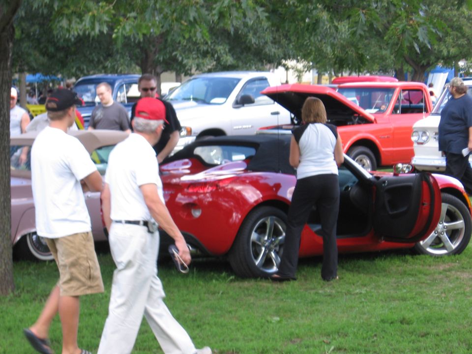Red convertible with door open, people around it