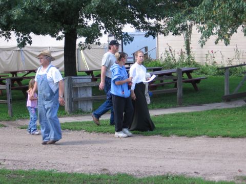 1989 Ford Mustang - A group of people walk past picnic tables and tents in an outdoor setting.