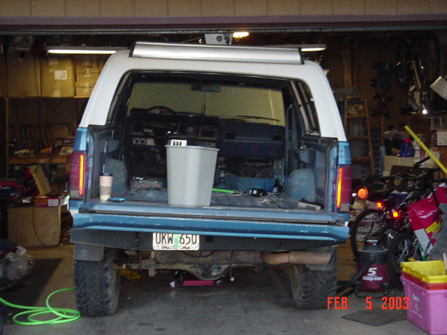 Rear hatch open on blue and white Ford Bronco inside a cluttered garage, plate UKW-650