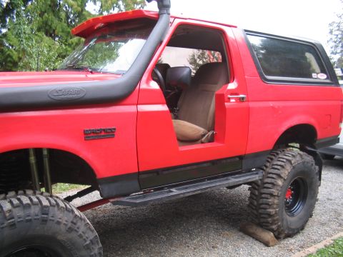 1989 Ford Bronco - This red Ford Bronco has a snorkel and large off-road tires, with the driver's side door removed.