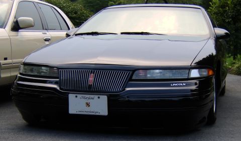 1996 Mercury Grand Marquis - A black Lincoln sedan is parked next to a tan vehicle, showing its front grille and headlights.