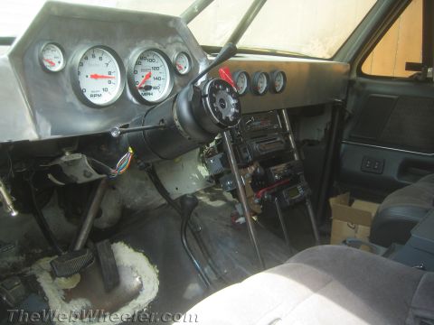 1990 Ford Bronco - Interior of a stripped vehicle showing an aluminum dash panel, Auto Meter gauges and an exposed steering column.