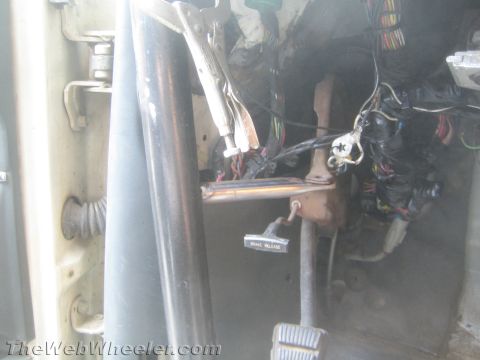 1990 Ford Bronco - Driver footwell of a stripped vehicle showing the brake pedal, a brake-release lever labeled tag and wiring.