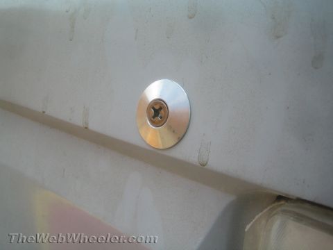1990 Ford Bronco - polished round fastener with a Phillips screw mounted on a dusty white body panel above a clearance light.