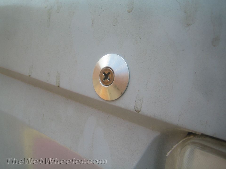 Polished round metal hood pin or fastener mounted on a dirty white body panel