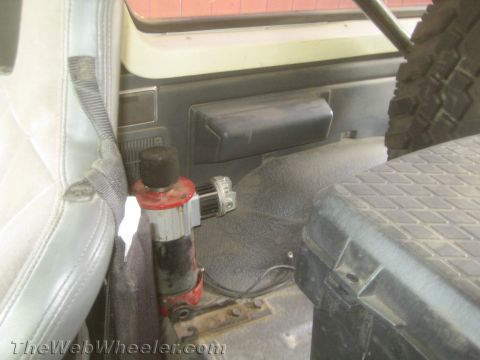 1990 Ford Bronco - red hydraulic lever bolted to the cab floor beside a worn light-gray seat, with a tire visible at right.